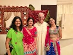 Nimisha Ladva stands with her daughter Himani Steingard, husband David Steingard and daughter Medha Steingard. The women are wearing brightly colored outfits, and everyone has big smiles.