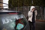 Felicia is talking on a cellphone outside of her car. She wears a hoodie with the hood pulled up.