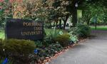 A sign reads "Portland State University," next to a sidewalk that runs through a lawn with trees and other plant life.