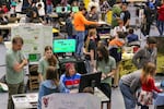 Several groups of students gather at different tables, and each team plays a game and gives a science fair-like presentation.