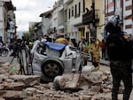 A police officer looks up next to a car crushed by debris after an earthquake shook Cuenca, Ecuador, on Saturday.