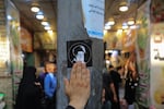 A pilgrim touches a sticker bearing a portrait of Iranian Supreme Leader Ali Khamenei affixed to a utility pole