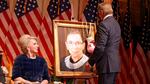 Sylvester Stallone hangs a pair of pink boxing gloves on a portrait of the late Supreme Court Justice Ruth Bader Ginsburg at the Justice Ruth Bader Ginsburg Woman of Leadership Award in 2022, as Julie Opperman, chair of the Dwight D. Opperman Foundation, looks on.