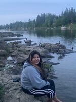 A teenager sits on rocks next to a lake or river, with her feet in the water.