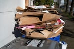 FILE: Cardboard packaging sits in a stack on top of a recycling bin outside a garage in Portland in 2026. Oregon lawmakers enacted a recycling system that shifts costs onto corporations, so they pay for the product packaging they bring to Oregon.