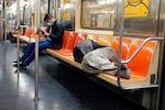 A person sleeps on the seats of a New York City subway train.