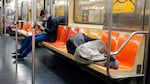 A person sleeps on the seats of a New York City subway train.