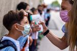 A teacher wearing a face mask to protect against the spread of coronavirus checks the temperature of her student.