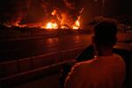 A man looks at flames rising from an oil storage facility after it appeared to have been struck by an Israeli strike in Tehran, Iran, early Sunday, June 15, 2025.