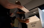 This photo shows a voter's arm and hand, with the hand holding a white envelope containing their ballot. The person is placing the envelope into a ballot box in Minneapolis on Sept. 20, and a second person is holding open the place where the voter slides in the ballot.