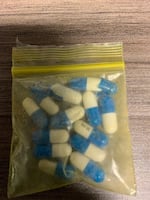 A plastic bag of white and blue capsule pills on a table.