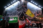 An Iranian demonstrator waves a flag of Lebanon's militant Hezbollah group under an anti-U.S. billboard depicting the American aircrafts into the Iranian armed forces fishing net with signs that read in Farsi: "The Strait of Hormuz will remain closed, The entire Persian Gulf is our hunting ground," during a pro-government gathering at Enqelab-e-Eslami, or Islamic Revolution, square in Tehran, Iran, Monday, May 4, 2026.