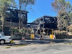 The charred exteriors of apartment buildings seriously damaged by fire, with firefighters standing outside.