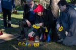 Paula Tin Nyo, flanked by her husband David Williams, left, and her son Kelland Harrison, places flowers on the grave of her son before it is disinterred.