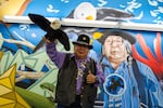 Ed Edmo, Shoshone-Bannock, holds up his stuffed bald eagle puppet as he poses for his photo in front of the  "A Place Called Home" mural inside the Portland airport, created by Portland artists Jeremy Nichols and Alex Chiu.