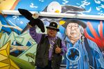 Ed Edmo, Shoshone-Bannock, holds up his stuffed bald eagle puppet as he poses for his photo in front of the  "A Place Called Home" mural inside the Portland airport, created by Portland artists Jeremy Nichols and Alex Chiu.