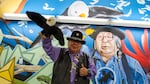 Ed Edmo, Shoshone-Bannock, holds up his stuffed bald eagle puppet as he poses for his photo in front of the  "A Place Called Home" mural inside the Portland airport, created by Portland artists Jeremy Nichols and Alex Chiu.