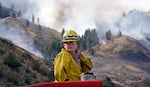 Firefighter Kathleen Calvin looks around as she sits atop her fire truck while waiting to begin work as smoke from a wildfire fills the sky behind Saturday, July 19, 2014, in Winthrop, Wash. A wind-driven, lightning-caused wildfire racing through rural north-central Washington destroyed about 100 homes Thursday and Friday, leaving behind solitary brick chimneys and burned-out automobiles as it blackened hundreds of square miles in the scenic Methow Valley northeast of Seattle.