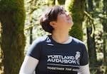 A young person looks up with trees in the background.