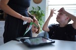 Charlie Lamb, right, who is diagnosed with autism and is non-verbal, uses an AAC device to communicate with his mother Eileen Lamb left, who also has autism, as Charlie's sister Billie looks on, Monday, May 12, 2025, in Austin, Texas.