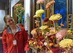 A woman in red jacket is holding a handle of a floral arrangement inside a room.