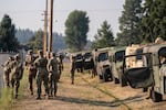 National Guard members in uniforms stand together and talk next to a row of parked military vehicles.
