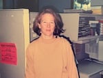 A woman stands in front of an office cubicle.