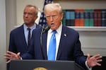 President Trump stands at the microphone at the White House in front of a shelf of books.