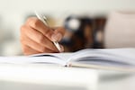 Close up of female hands writing notes in her diary while staying at home