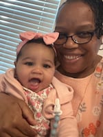 Yalanda Lattimore, 59, holds her 1-year-old granddaughter, Mavee. Lattimore is smiling, and Mavee has her mouth wide open. Mavee is dressed in pink, and around her head she's wearing a pink headband with a bow.