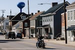 Two people on a motorcycle ride down a road in Williamsport, Maryland, on March 9. Two- and three-story buildings line the street behind them.