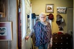 Suzann Roberts, 90, stands in her home in Ann Arbor, Michigan. She has short gray hair and is wearing glasses. She has a colorful poncho over a gray sweater.