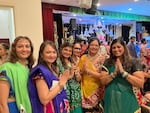 Women in brightly colored clothes gather together at the Bharatiya Temple’s Navaratri celebration in Chalfont, Pennsylvania, some with their hands pressed together in front of them.