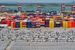 Chinese-made cars are lined up in rows at the port in Nanjing, China. Behind the cars are stacks of cargo shipping containers in a variety of colors — blue, red, yellow, brown, orange.