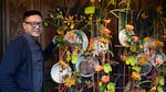 A man with glasses stand next to a floral installation.