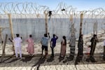 Relatives and friends wait by a fence topped with barbed-wire for the return of people who had previously crossed into Spain's North African enclave of Ceuta, at Morocca's Bab Sebta border crossing on the outskirts of Fnideq on August 2, 2026.