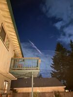 What looks like a shooting comet is visible in the evening sky over a backyard that includes a tall, wood privacy fence and a second-floor deck.