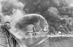 Firemen stand on a bridge over the Cuyahoga River and spray an arc of water on the tug Arizona as a fire engulfs the docks in Cleveland on Nov. 1, 1952. Smoke billows in the background. 