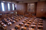 The floor of the Oregon House of Representatives shows desks aligned in rows facing other desks and a podium.