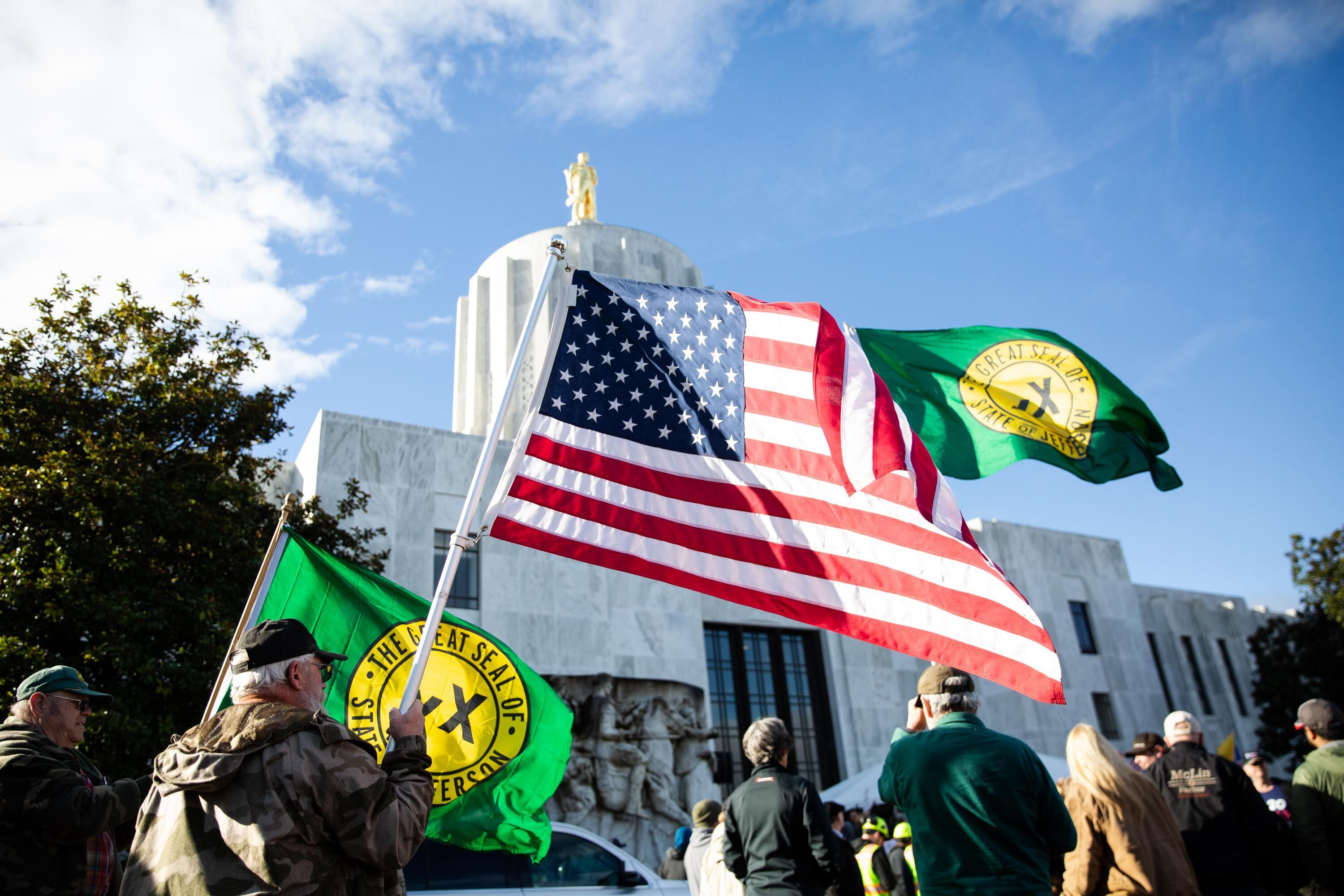 Men raise United States and State of Jefferson flags outside the Capitol in Salem, Ore., during a Timber Unity rally Thursday, Feb. 8, 2020. The rally was convened to oppose a cap-and-trade bill being proposed by Democrats that year.
