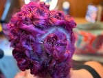 The back of a woman's head. Her hair is died purple, and it's rolled up into curls and pinned with bobby pins.