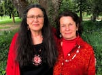 Two women, both wearing red, stand side by side at a park in front of a tree. They organized an event to recognize murdered and missing Indigenous women and girls.