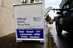 A person in a car reaches out to drop a ballot in the slot of a Multnomah County ballot box