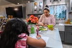 Lusely Martinez cuts vegetables at her kitchen island while her daughter sits at the island and draws.