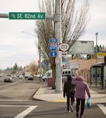 Pedestrians cross a street at an intersection near a sign that points to the Interstate 205 on-ramp.