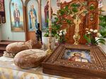 A small table on which there are two loaves of bread, a bottle of wine, a candle stick in a gold holder, an ornate golden crucifix, and a portrait of Jesus Christ.