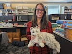 A woman holds a white cat doll inside a library.
