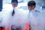 TOPSHOT - This picture taken on July 23, 2015 shows sales staff exhaling vapour while demonstrating their electronic cigarette products at the Beijing International Vapor Distribution Alliance Expo, or the Vape China Expo, at the China International Exhibition Center in Beijing.