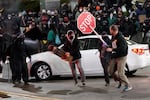 Protesters chase a street preacher, right, who was using a loudspeaker to deliver a sermon during a protest against police brutality, Sunday, Jan. 24, 2021, in downtown Tacoma, Wash., south of Seattle. The protest came a day after at least two people were injured when a Tacoma Police officer responding to a report of a street race drove his car through a crowd of pedestrians that had gathered around him. Several people were knocked to the ground and at least one person was run over.