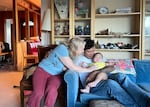 A woman sitting on a chair leans over and pats a baby being held by a man who sits on a sofa.